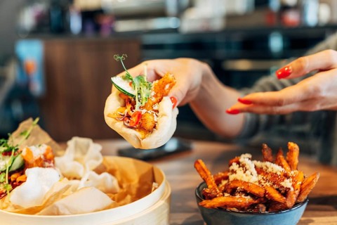 Woman enjoying fresh bao buns with crispy fries in a stylish restaurant