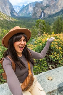 Woman smiling and gesturing at expansive yosemite valley from tunnel view, with bridalveil fall, el