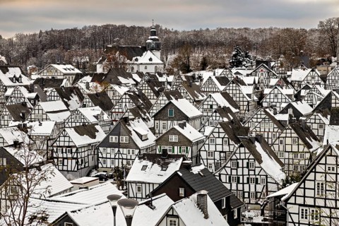 Close-up of snow-covered half-timbered houses and a church in the background, nestled in a wintery