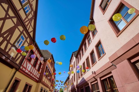 Colourful lanterns hang over a sunny road between half-timbered houses, Lohr am Main,