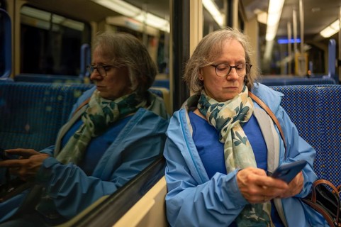 Interior view, elderly woman, glasses, sitting in S-Bahn, subway, train, typing on smartphone, cell