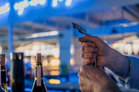 Men's hands open a bottle of wine at the bar. A close-up shows a sommelier's hands opening a wine