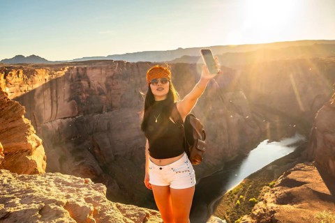 Young woman standing on the edge of a cliff at horseshoe bend, taking a selfie with her phone,