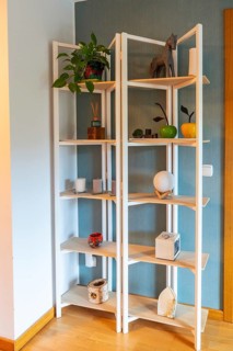 Wooden shelving unit with white frame filled with plants, candles, diffusers, and decorative