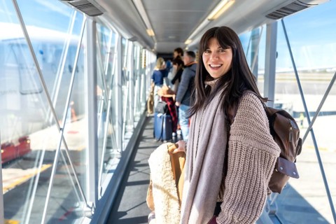 Happy woman passenger in warm clothing looking at camera, standing inside a modern jet bridge,