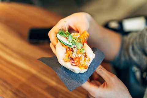 Woman Holding a Bao Bun with Fresh Ingredients in a Casual Restaurant Setting