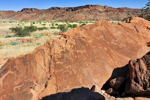 Rock carvings in an African savanna landscape with mountains and vegetation in the background, The