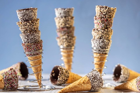 Ice cream cones stacked in metal stands, decorated with sprinkles and nuts