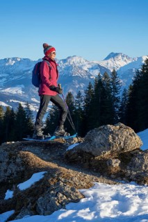 Nice and active senior woman snowshoeing in in the snow covered Allgaue alps above the valley of