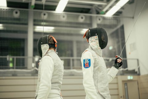 Two fencers are standing back to back in a sports hall and are ready for the next assignment,