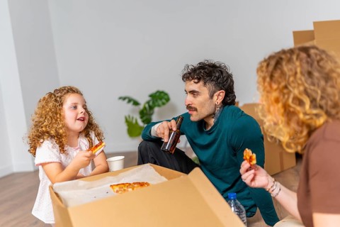 Family, including a father, mother, and daughter, sitting on the floor, enjoying pizza and drinks