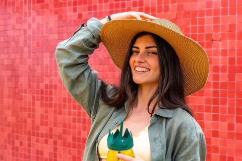 Young woman smiling while posing with a sun hat and a refreshing pineapple shaped drink, standing