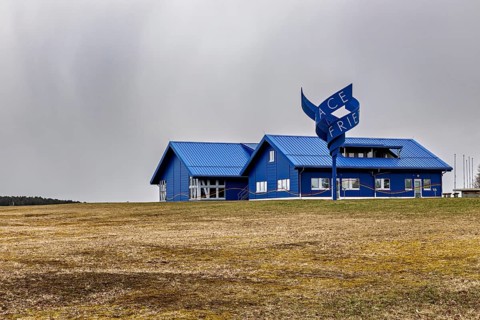 Modern blue building with a wavy sign on a field under cloudy sky, The Point Alpha memorial between