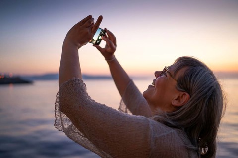 Woman with cell phone taking selfie at sunset, Strait of Messina, Calabria, Aeolian or Aeolian