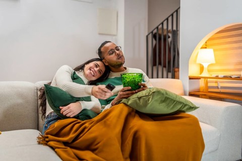 Young couple enjoying a cozy movie night together on the sofa, eating popcorn and watching
