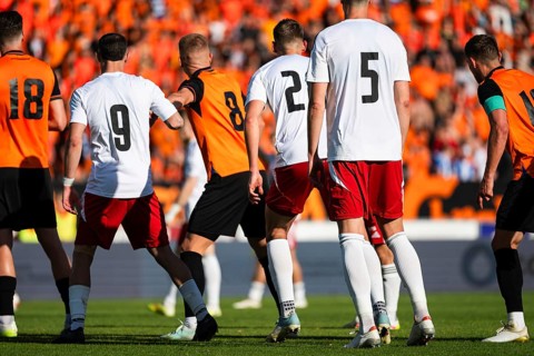 Professional soccer players in white and orange uniforms standing on the pitch during an intense