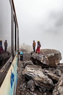 People in safety equipment on foggy cliffs next to a bus, adventurous atmosphere, rock slide on the