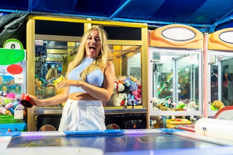 Young woman laughing with excitement while playing a claw machine and air hockey at an amusement