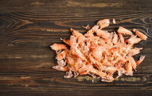 Shrimp shells on a wooden table. This shows a process of peeling and preparing shrimp for cooking.