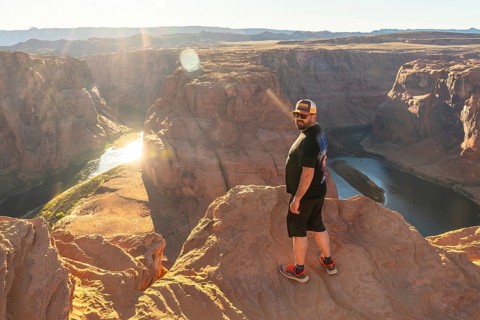 Man stands on a cliff edge overlooking horseshoe bend and the colorado river at golden hour, warm