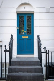 Blue front door with gold fittings and stained glass panes in white house facade surrounded by