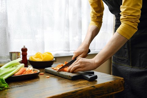 In a kitchen with natural light, a person is chopping carrots on a wooden cutting board. Fresh