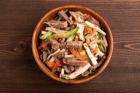 Meat salad with beef and vegetables in wooden bowl on brown wooden background. top view, flat lay,