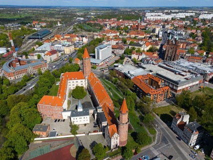 Aerial view of a castle complex with distinctive towers surrounded by cities and green areas,