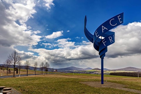 Peace sculpture in a meadow under a cloudy sky with hilly landscape in the background, The Point