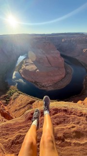 Adventurous traveler dangling legs over the edge of horseshoe bend canyon, showcasing the vast