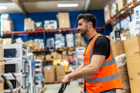 Warehouse employee wearing a safety vest and pushing a trolley, transporting goods and supplies