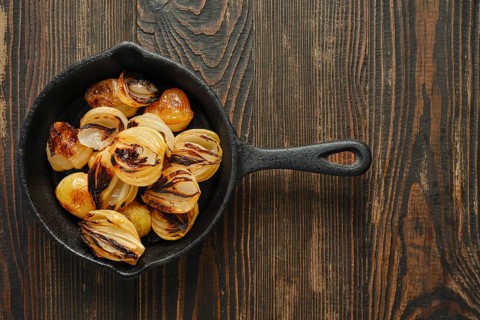Top view of cast iron skillet with roasted onions on wooden table. Onions show grill marks and