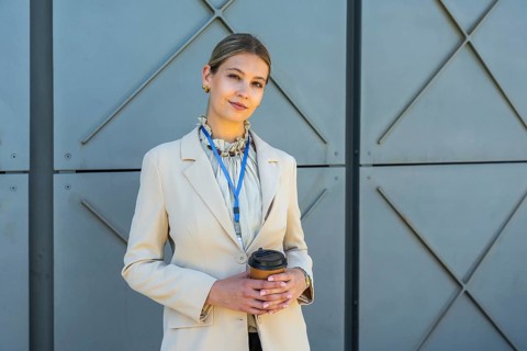 Young businesswoman wearing a blazer and a lanyard, confidently standing outdoors against a modern
