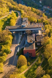 Aerial view of a modern building nestled in a green landscape with roads and trees under sunny