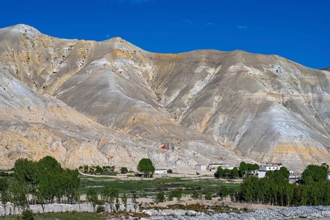 Small settlement and cultivated fields in front of mountainous landscape, erosion landscape near Lo