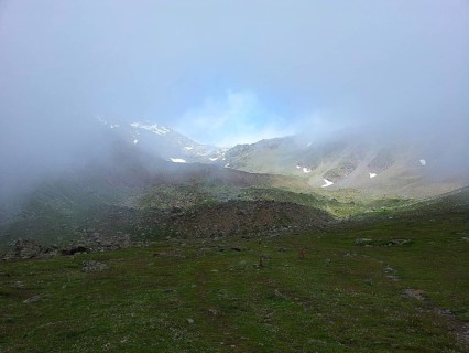 Cloudy mountain landscape with meadows and small snow-covered areas, E5, hiking in the Alps,
