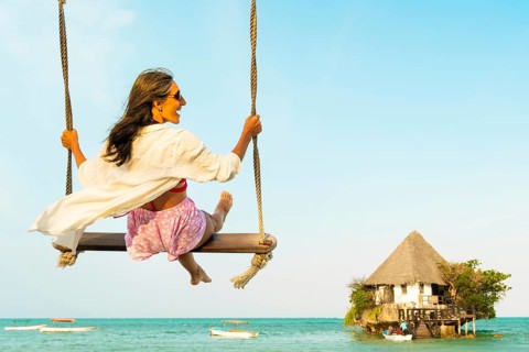 Carefree excited Middle aged woman tourist in pink sarong relaxes on beach swing overlooking the