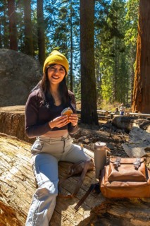 Woman sitting on a fallen log and eating a sandwich while taking a break during a sunny hike