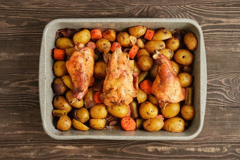 Rabbit meat and assorted vegetables are cooking together in a baking dish. The dish sits on a