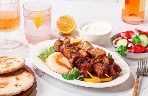 Souvlaki, a Greek dish, grilled meat shish kebab, on a plate with flatbreads, and lemon slices,