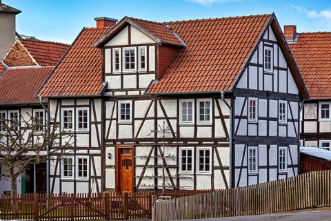 Traditional half-timbered house with red tiled roof and wooden fence against a clear sky, historic