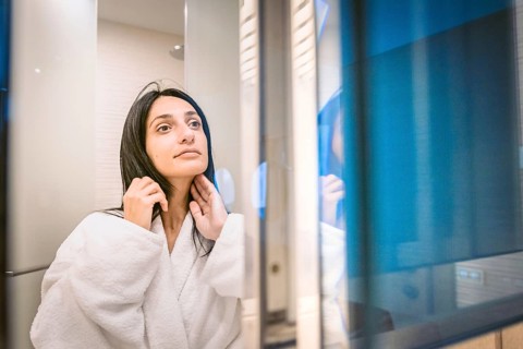 Pretty woamn brushes her hair and looks to her bright clear skin in the mirror with reflection