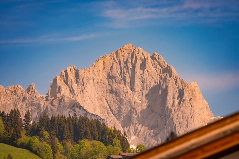 Rocky mountain peak against blue sky surrounded by trees and green hills, Hahnenkamm, Kitzbühel,