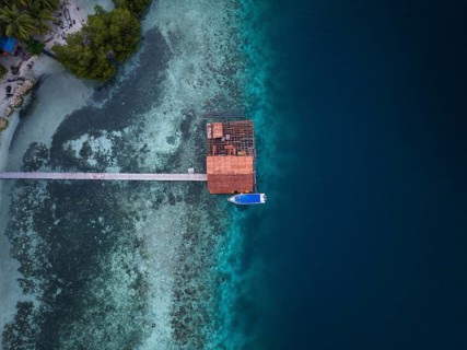 Aerial view from top to bottom of a jetty and a boat and a presented reef, Raja Ampat, West Papua,