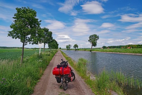 Cycling on a narrow canal path with a landscape of water and trees under a blue sky, bicycle tours,