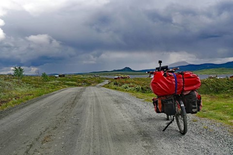 Bicycle with luggage on a dirt road under dramatic cloud formations, bicycle route, Jotunheimvegen,