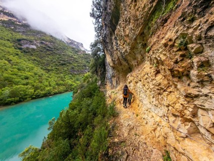 Woman and child hiking a narrow path carved into a steep rock cliff face, staying close to the