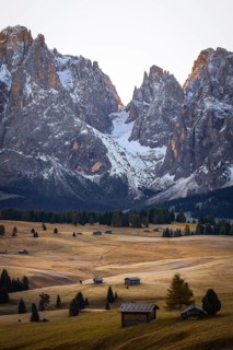 High snow-covered mountains over quiet meadows strewn with huts, view over the autumnal Seiser Alm