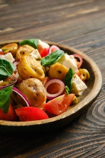 Close-up view of warm potato and feta salad is served in wooden bowl. It includes potatoes, feta