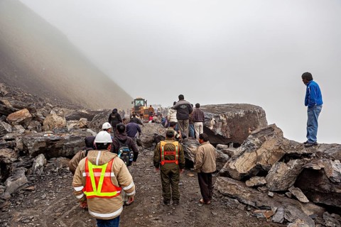 People work on a large, rocky construction site in fog, rockslide on the pass road towards